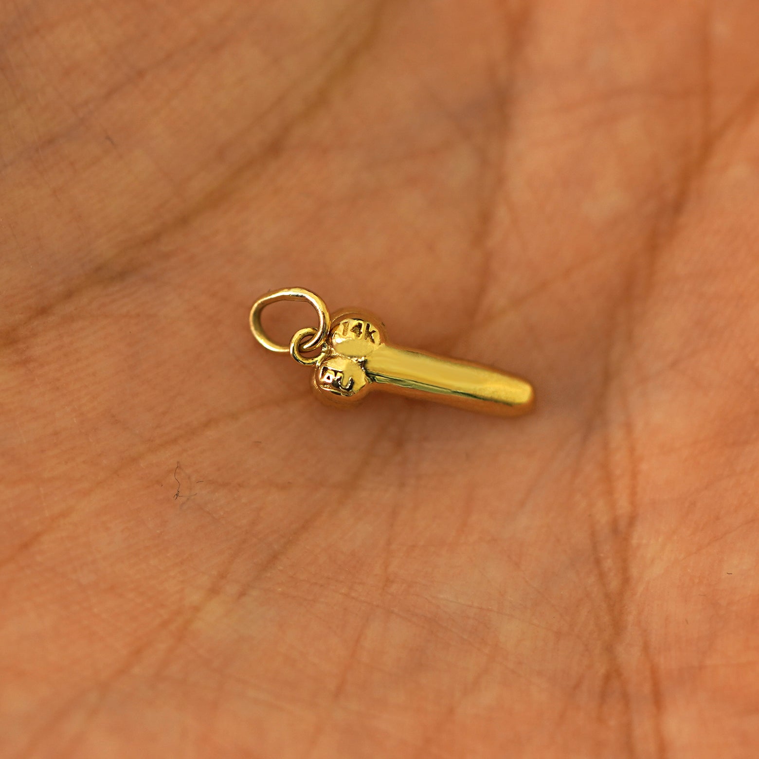 Another angle of a 14k yellow gold penis charm in the palm of a models hand
