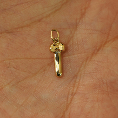 A 14k yellow gold penis charm in the palm of a models hand