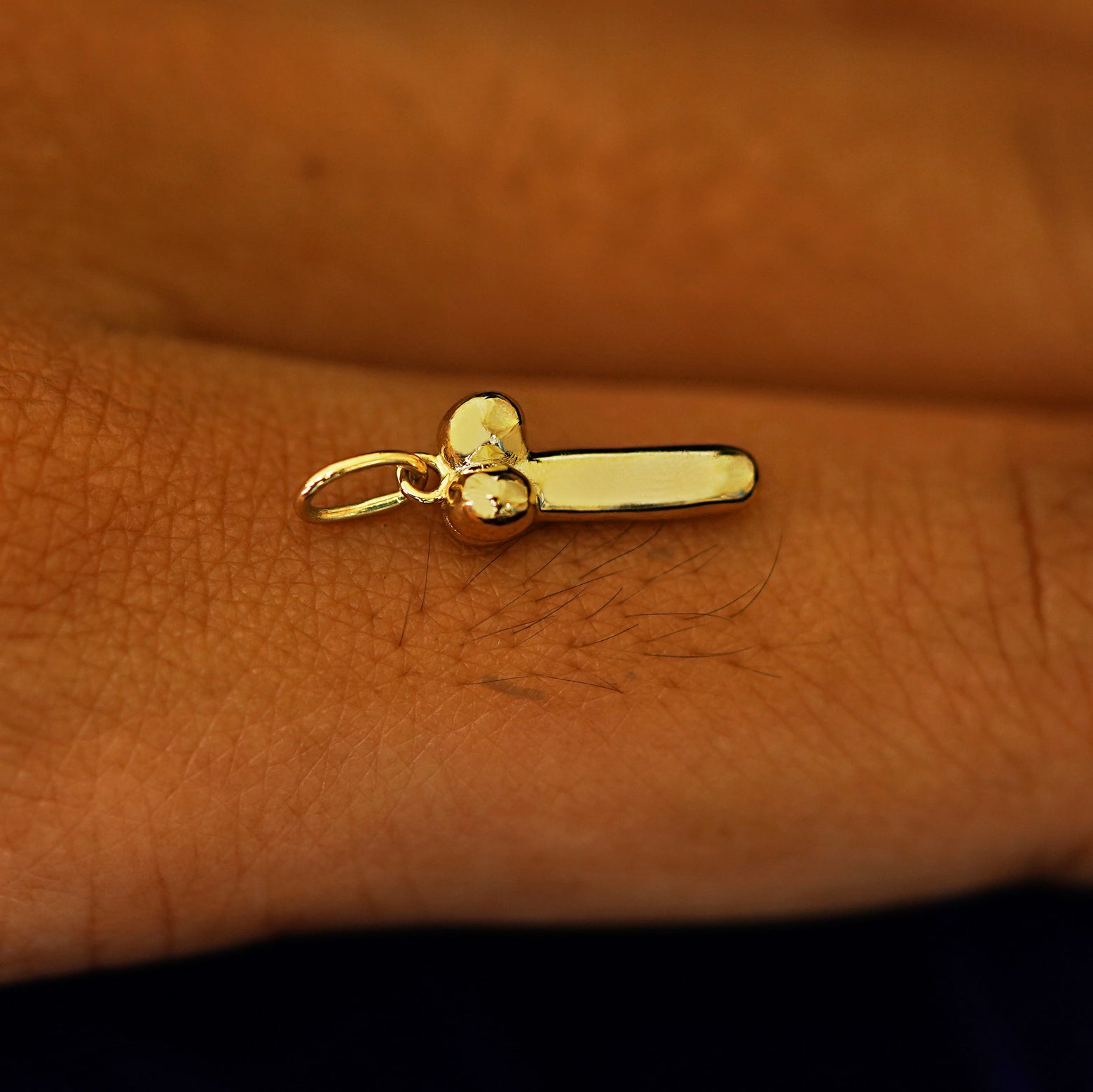 Side view of a 14k yellow gold penis charm on the back of a models finger 