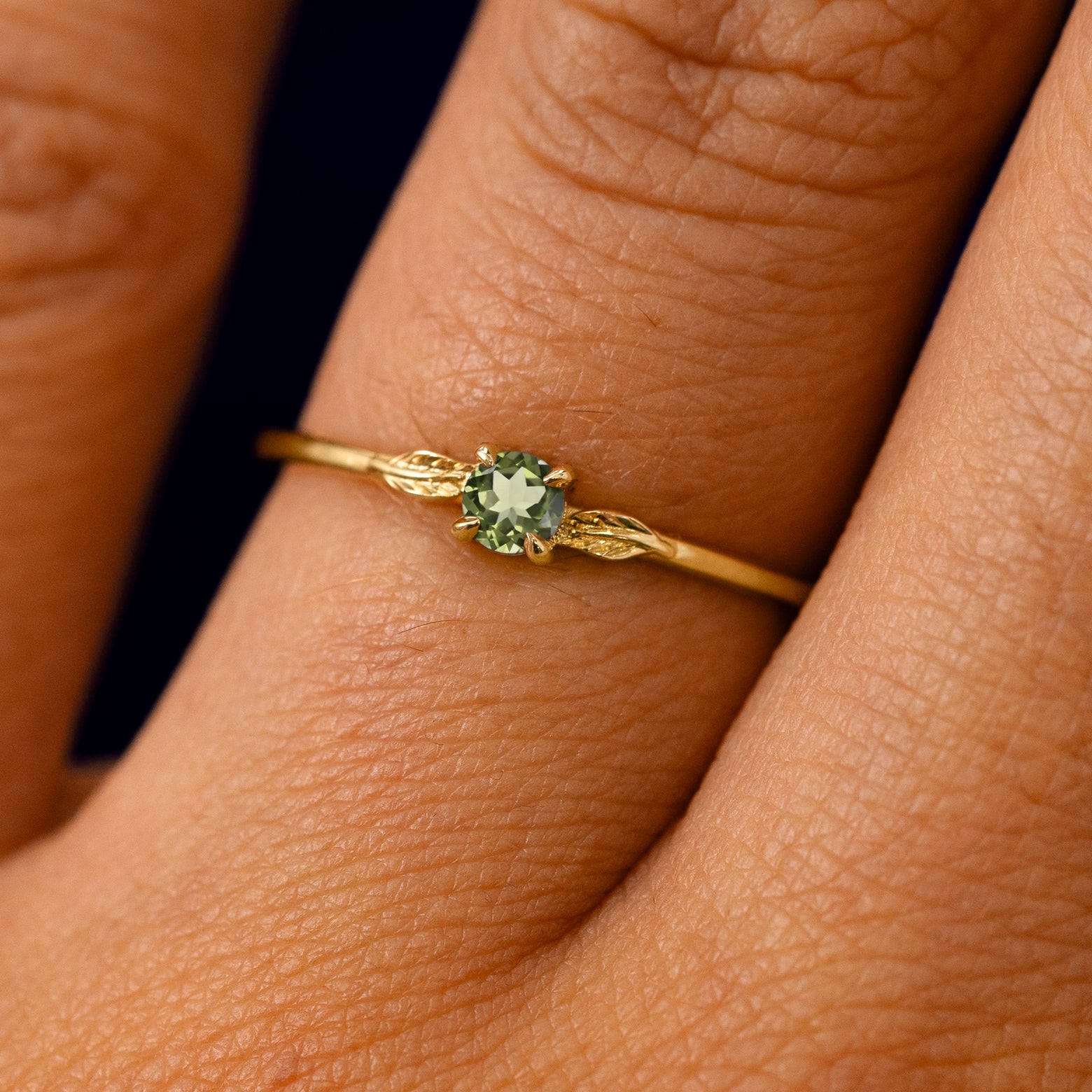 A solid 14k yellow gold Peridot Gemstone Two Leaf Ring on a model's finger
