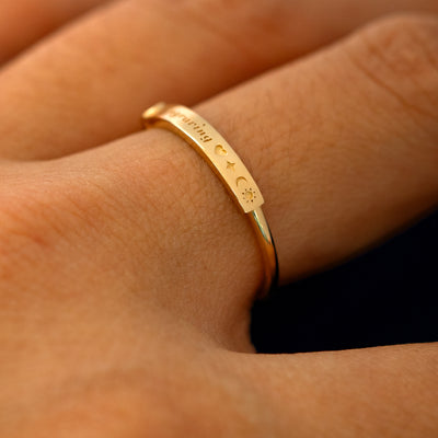 A model wearing a bezel set gemstone bar ring to show the cursive lettering and engraved heart star sun and moon on the bar