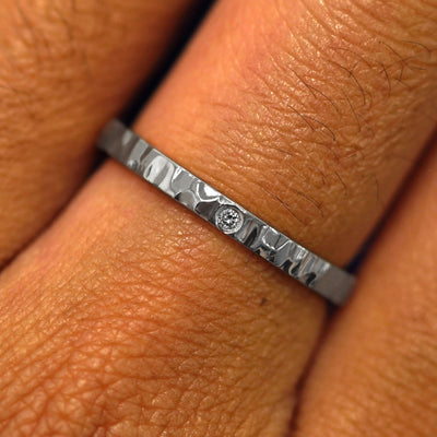 Close up view of a model's fingers wearing a Platinum Industrial Hammered Band with one diamond