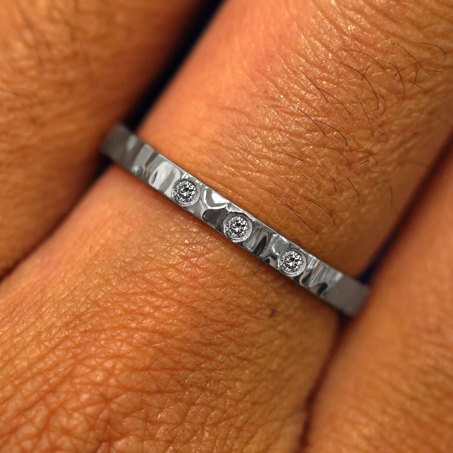 Close up view of a model's fingers wearing a Platinum Industrial Hammered Band with three diamonds