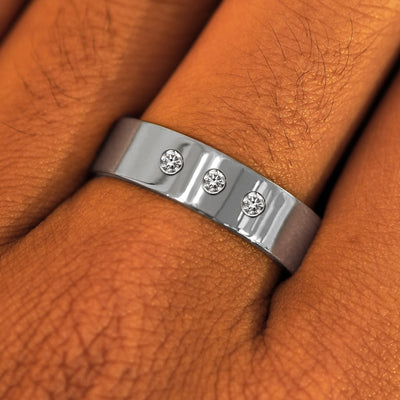 Close up view of a model's fingers wearing a 6mm Platinum Industrial Mirror Band with three diamonds