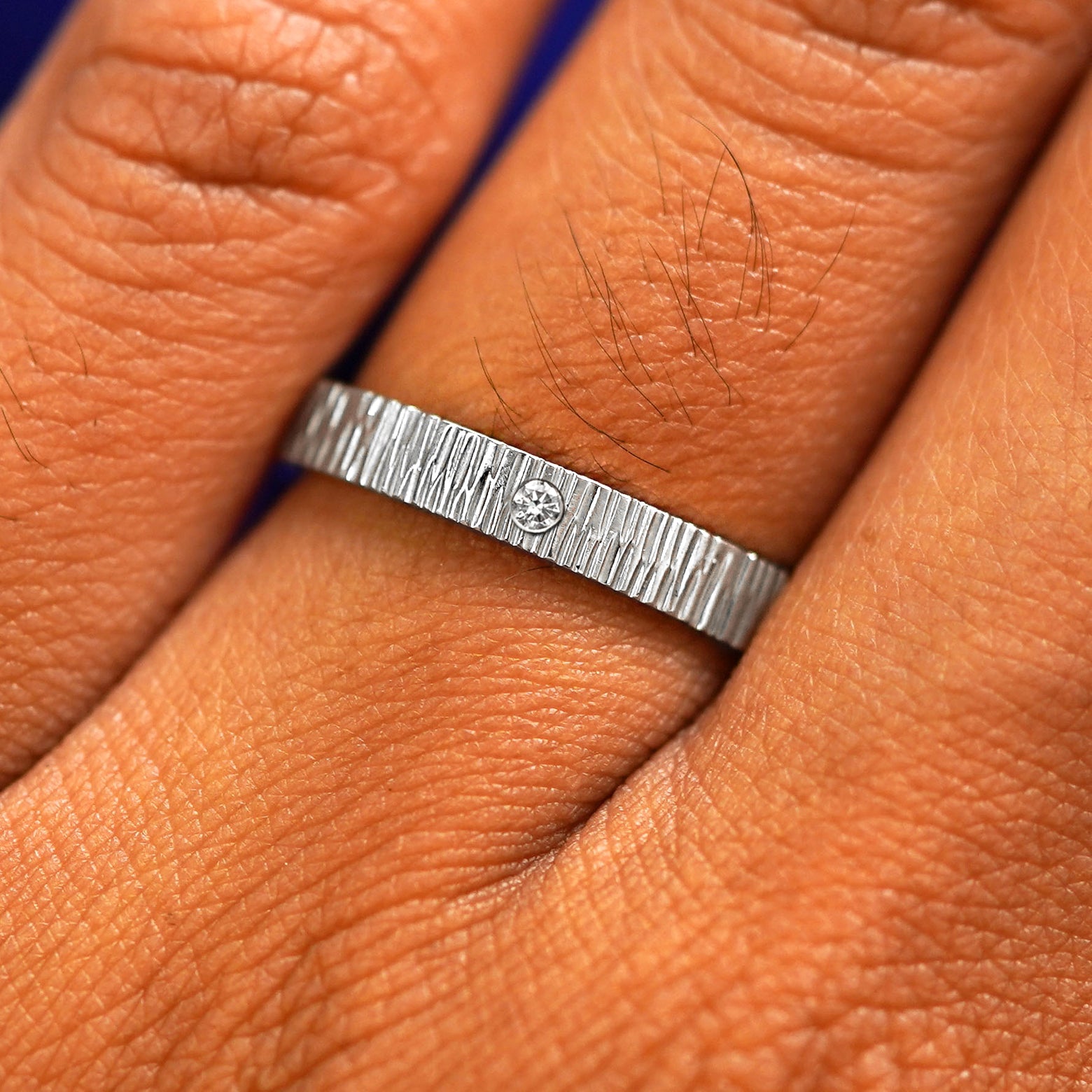 Close up view of a model's fingers wearing a Platinum Industrial Wood Band with one diamond