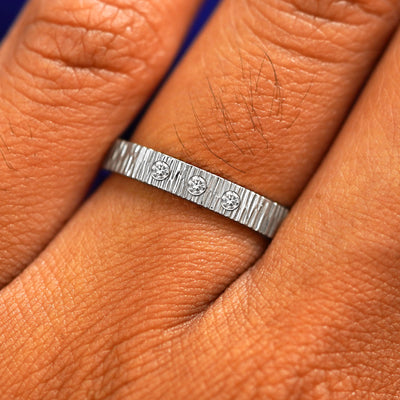 Close up view of a model's fingers wearing a Platinum Industrial Wood Band with three diamonds