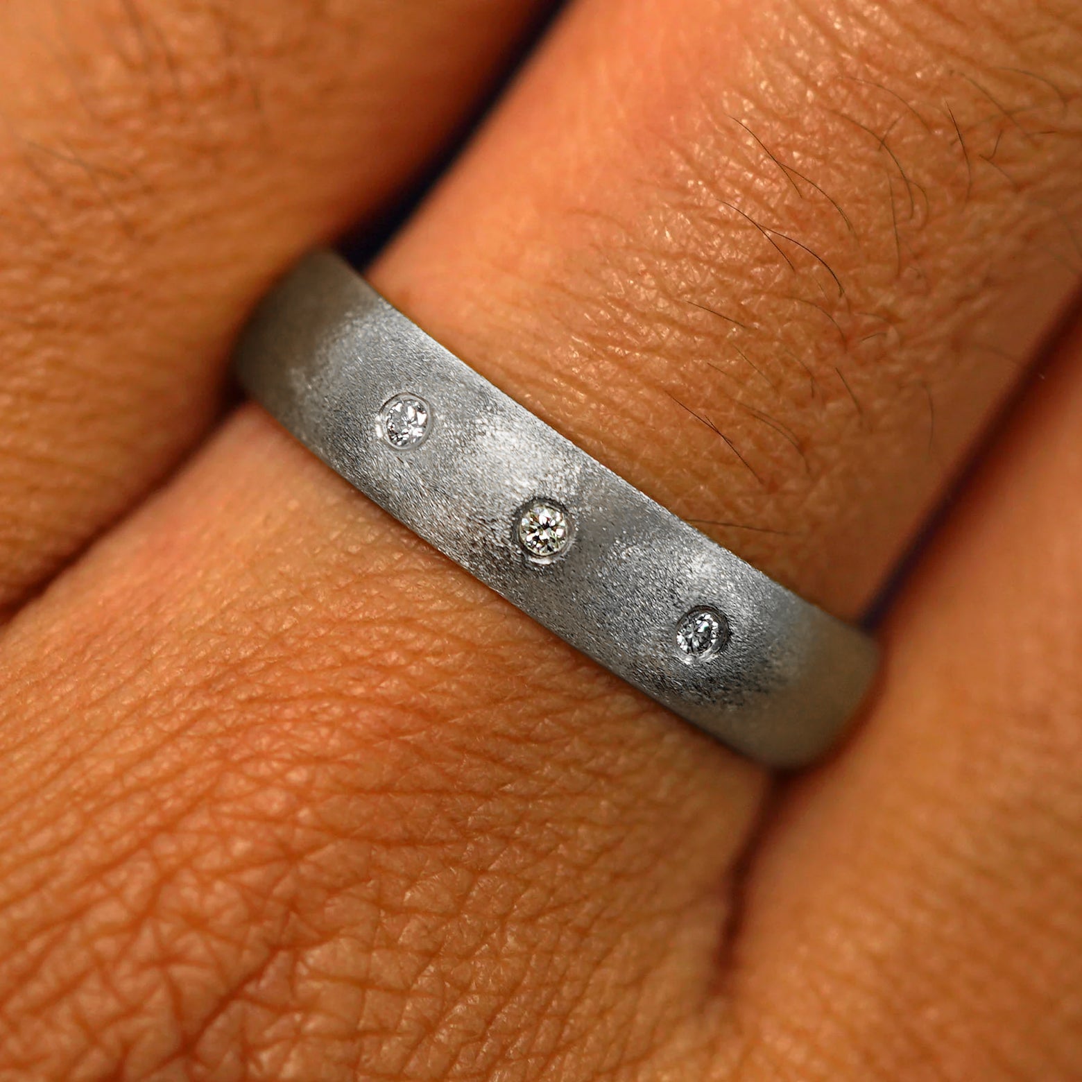 Close up view of a model's fingers wearing a 4mm 925 silver Curvy Matte Band with three diamonds