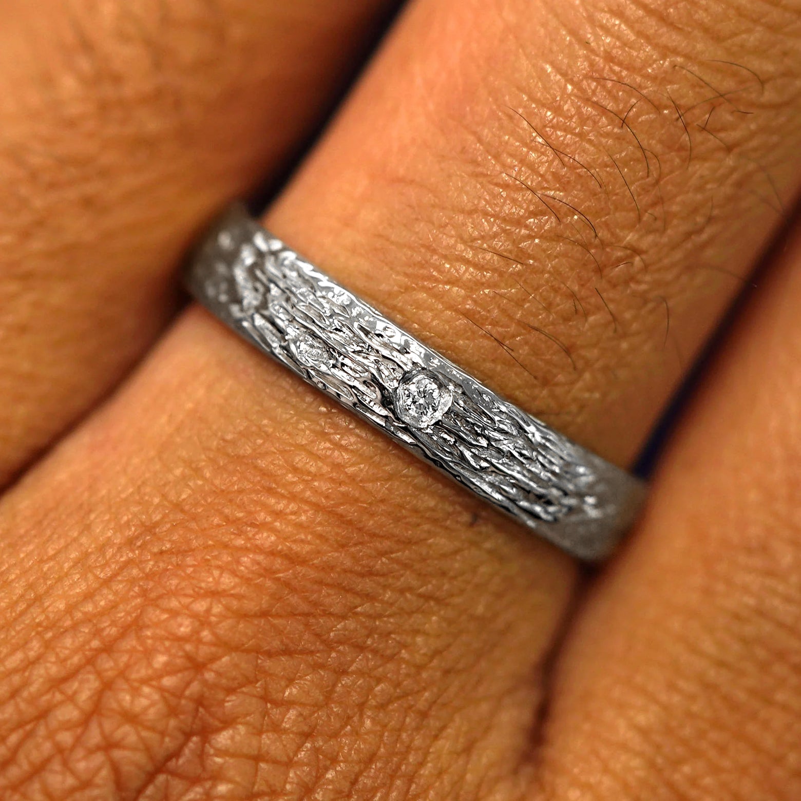 Close up view of a model's fingers wearing a Platinum Raw Band with one diamond