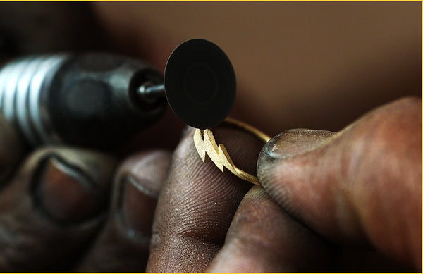 A jeweler uses a rotary polishing tool to polish a yellow gold Lighting Bolt Ring