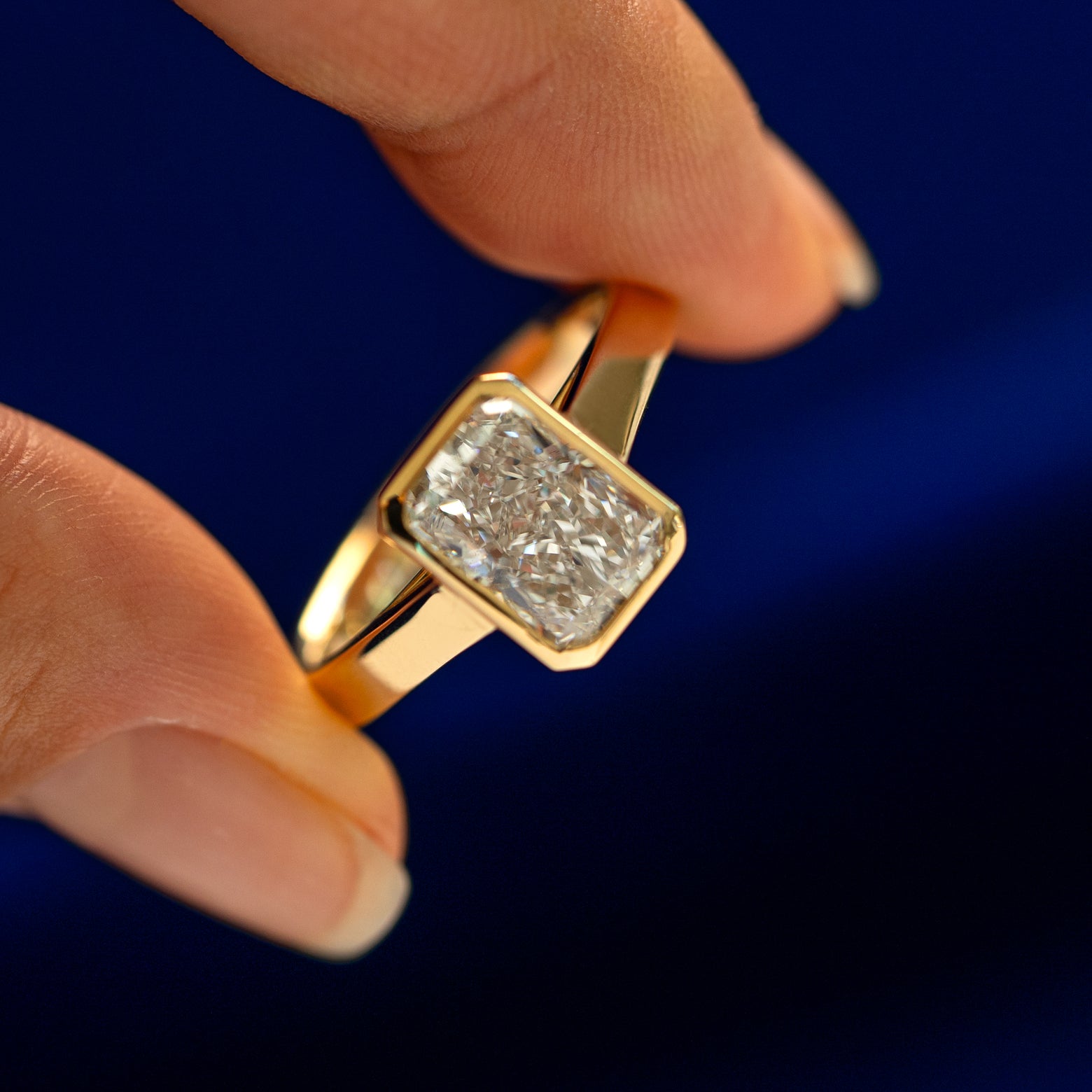 An angled view of a Radiant Cut Lab Diamond Cathedral Ring on a model's finger to show the bezel setting