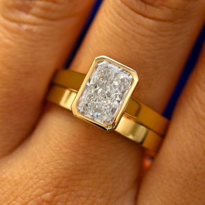 A model's fingers wearing a 14k yellow gold Radiant Cut Lab Diamond Cathedral Ring with Industrial Mirror Band