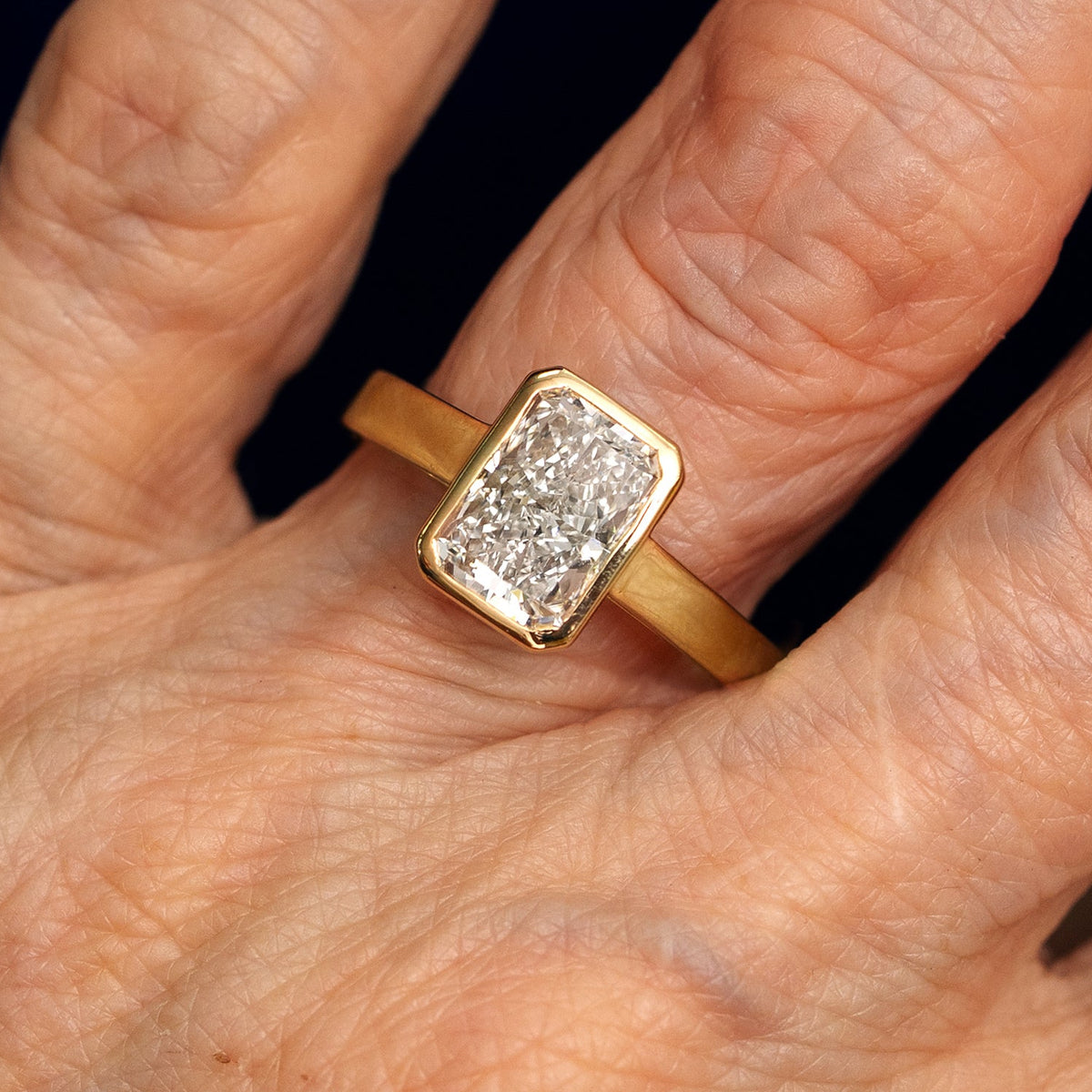 A solid 14k yellow gold Radiant Cut Lab Diamond Cathedral Ring on a model's finger