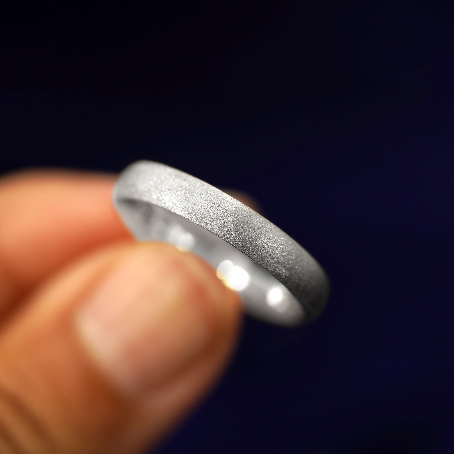A model holding a Silver Curvy Stardust Band tilted to show the details of the star dust finish