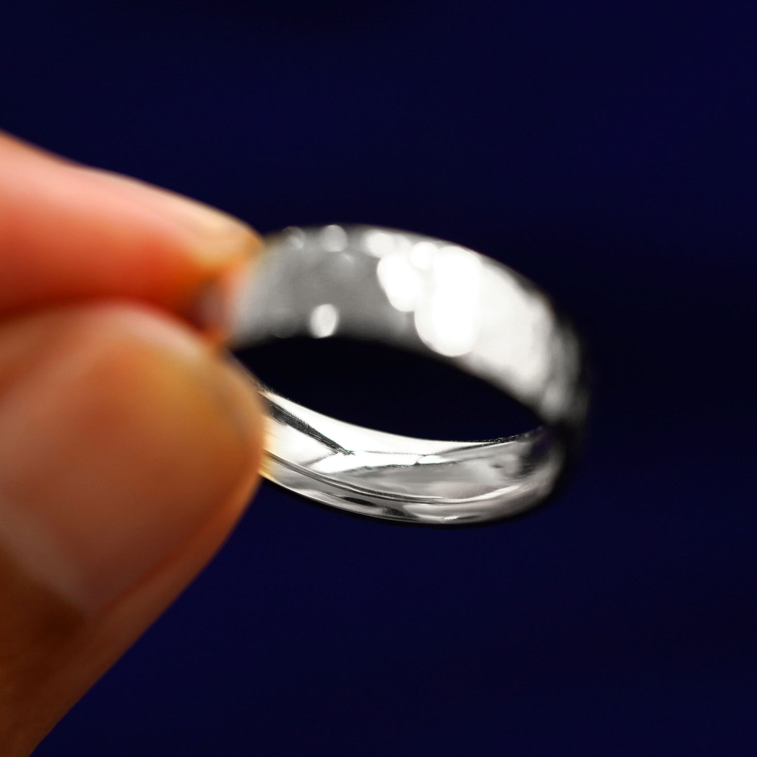 A model holding a Silver Industrial Hammered Band tilted to show the inside of the band