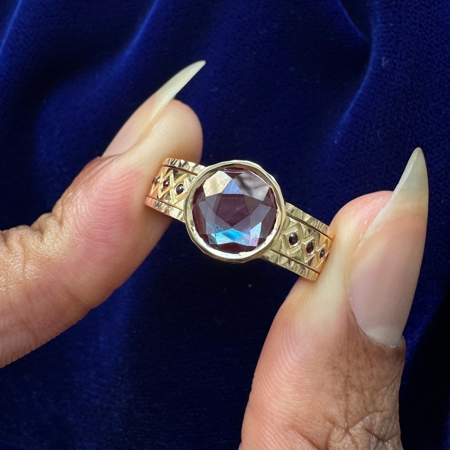 A model holding a custom cut alexandrite engagement ring that acts as a reverse ring guard to a wedding band with garnets