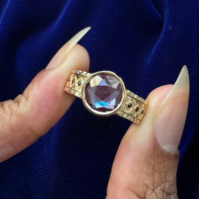 A model holding a custom cut alexandrite engagement ring that acts as a reverse ring guard to a wedding band with garnets