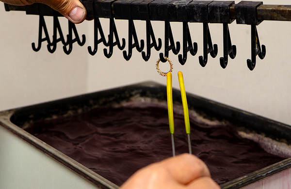 A solid gold diamond eternity band on a hook over an ultrasonic cleaning bath
