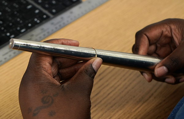 An Automic Gold employee using a metal ring sizer to accurately measure a thin gold ring