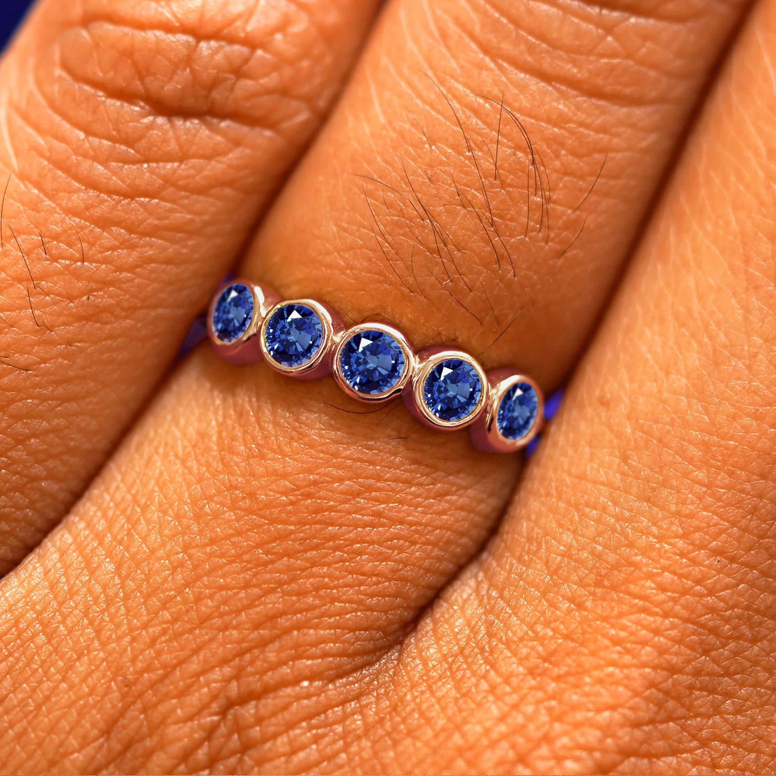Close up view of a model's hand wearing a rose gold 5 Gemstones Ring in sapphires