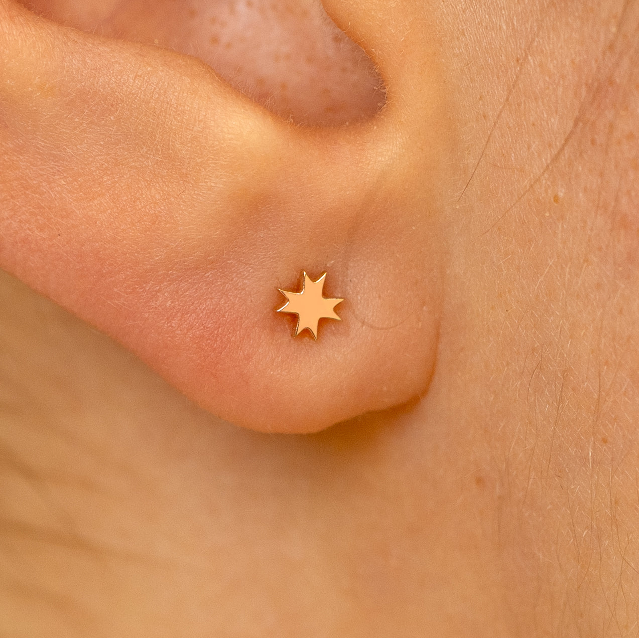 Close up view of a models ear wearing a 14k rose gold 8 pointed star flatback piercing