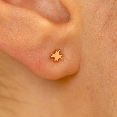 Close up view of a models ear wearing a 14k rose gold 8 pointed star flatback piercing
