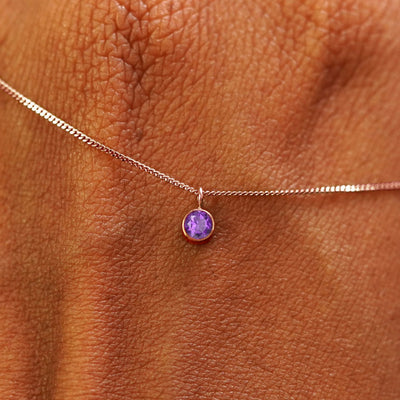 Close up view of a 14k rose gold Amethyst Necklace draped across the back of a model's hand