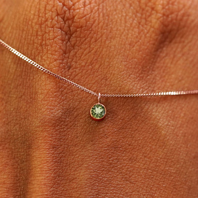 Close up view of a 14k rose gold Peridot Necklace draped across the back of a model's hand