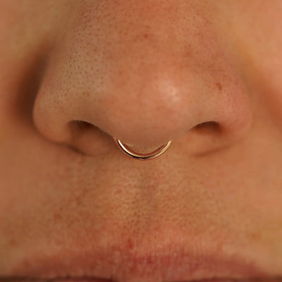 Close up view of a model's nose wearing a 14k rose gold Small Seamless Huggie Hoop in a septum piercing