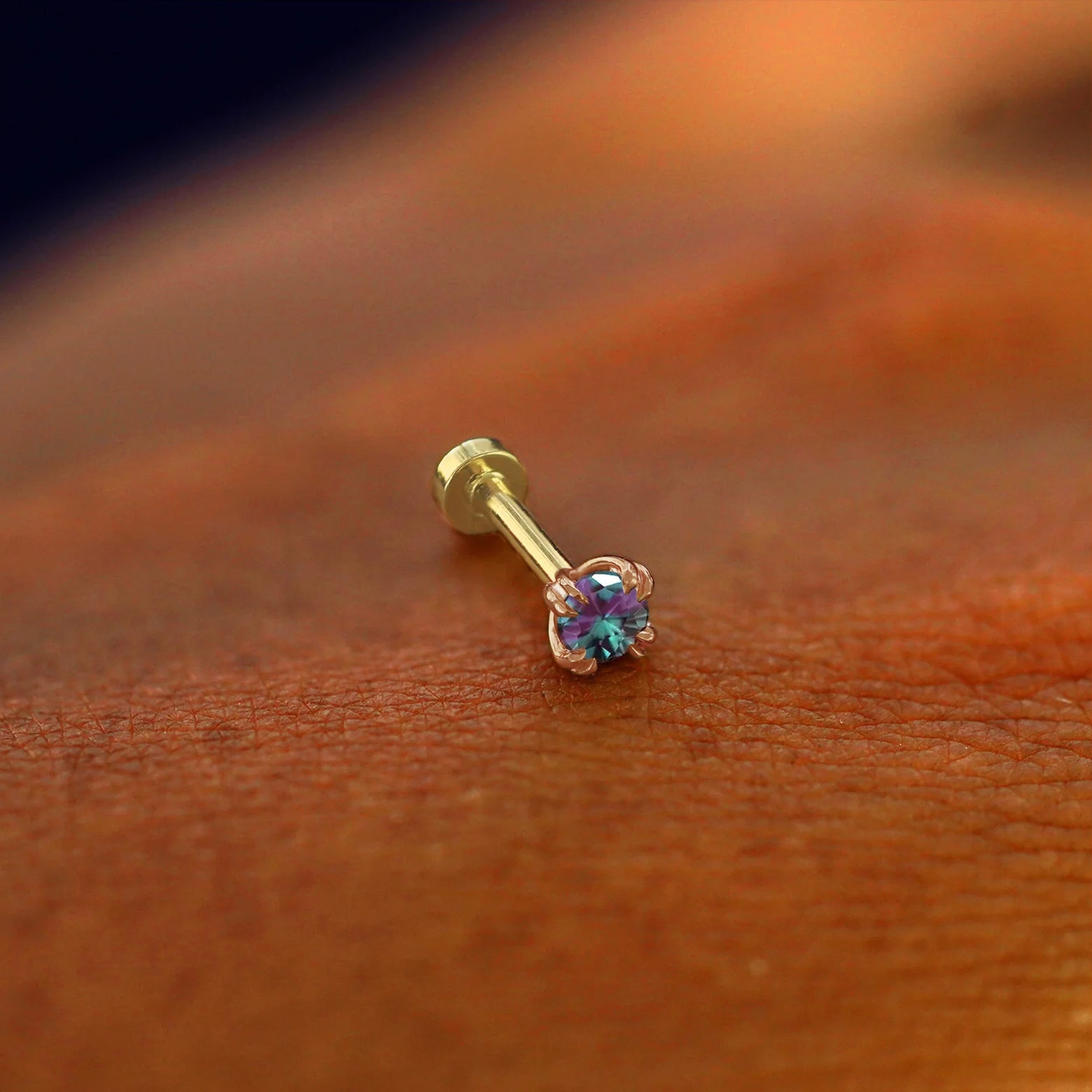 A solid 14k rose gold Alexandrite Flatback Piercing resting on the back of a model's hand