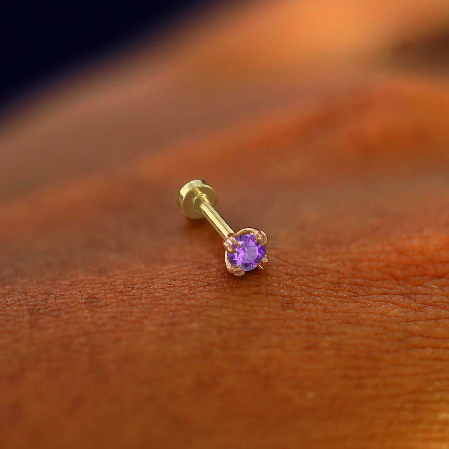 A solid 14k rose gold Amethyst Flatback Piercing resting on the back of a model's hand
