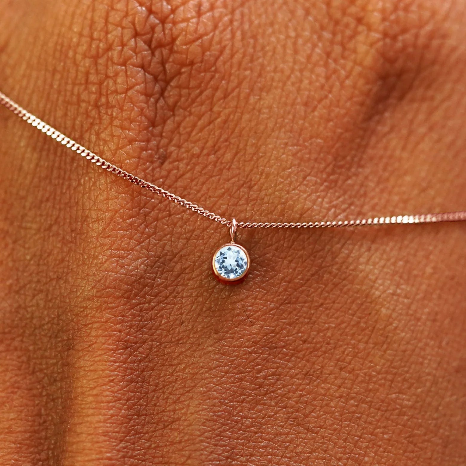 Close up view of a 14k rose gold Aquamarine Necklace draped across the back of a model's hand