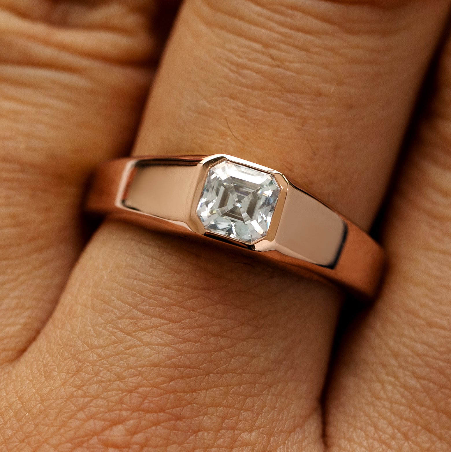 Close up view of a models hand wearing a 14k rose gold asscher lab gemstone ring