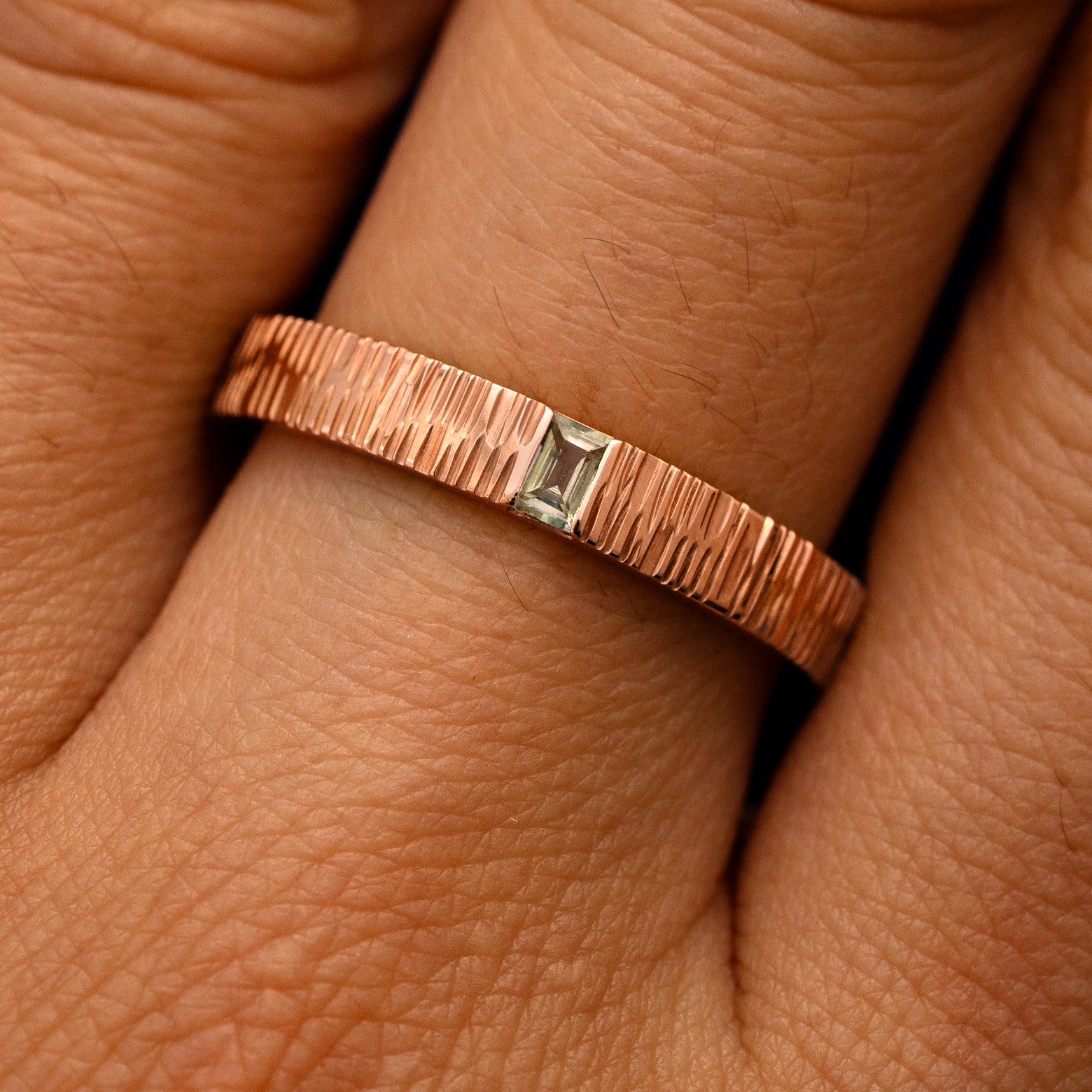 Close up view of a model's fingers wearing a 14k rose gold Baguette Green Sapphire Wood Band
