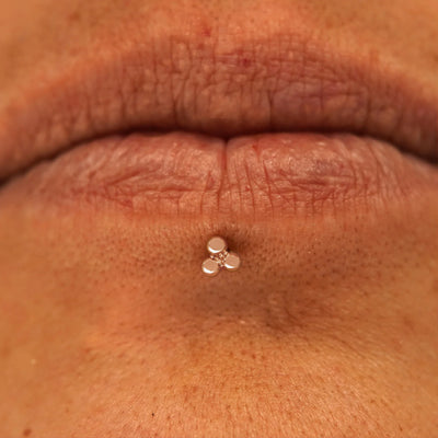Close up view of a model's mouth wearing a 14k rose gold Ball Trio Flatback as a labret piercing