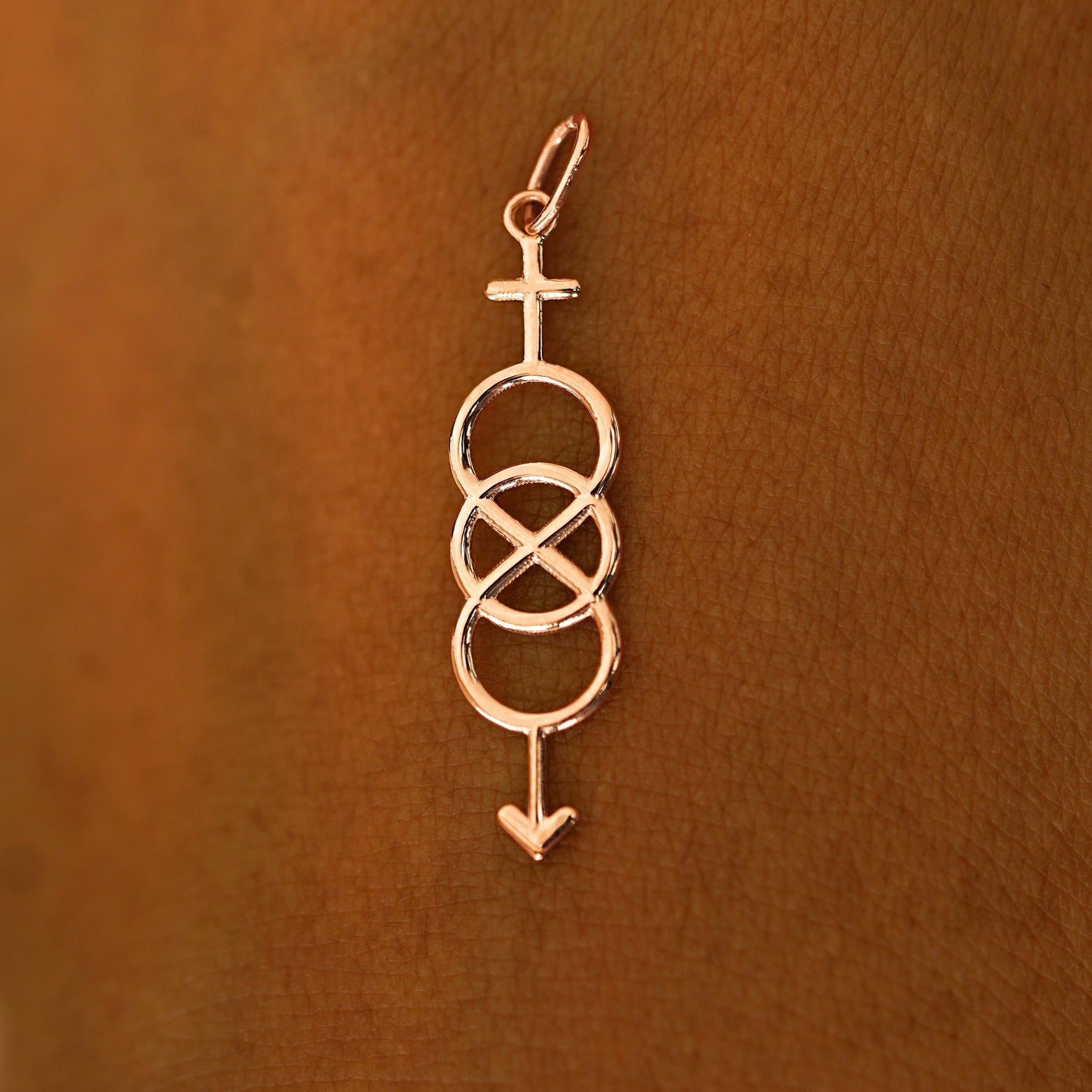 A solid 14k rose gold Bisexual Symbol Charm resting on the back of a model's hand