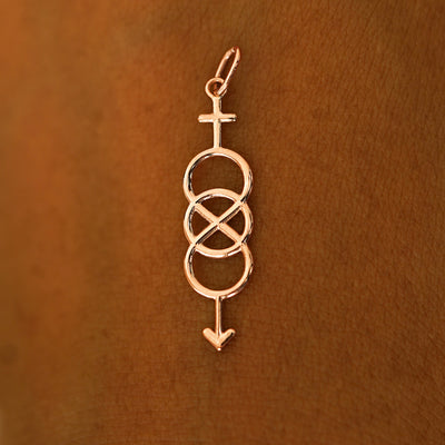 A solid 14k rose gold Bisexual Symbol Charm resting on the back of a model's hand