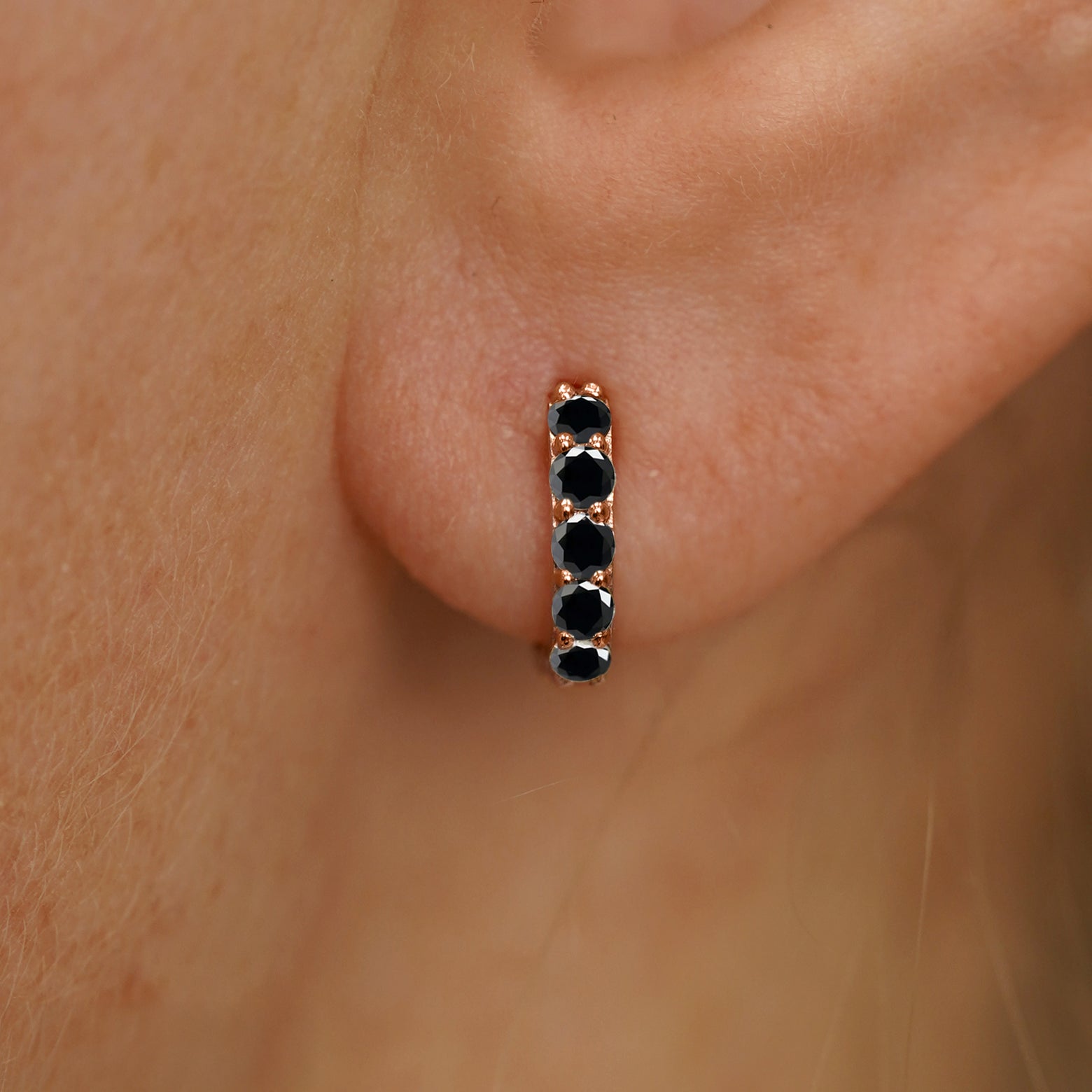 Close up view of a model's ear wearing a rose gold Mini Black Diamond Huggie Hoop