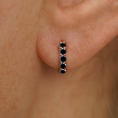 Close up view of a model's ear wearing a rose gold Mini Black Diamond Huggie Hoop