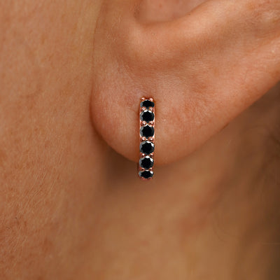 Close up view of a model's ear wearing a rose gold Small Black Diamond Huggie Hoop