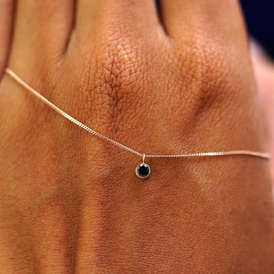 Close up view of a 14k rose gold Black Diamond Necklace draped across the back of a model's hand