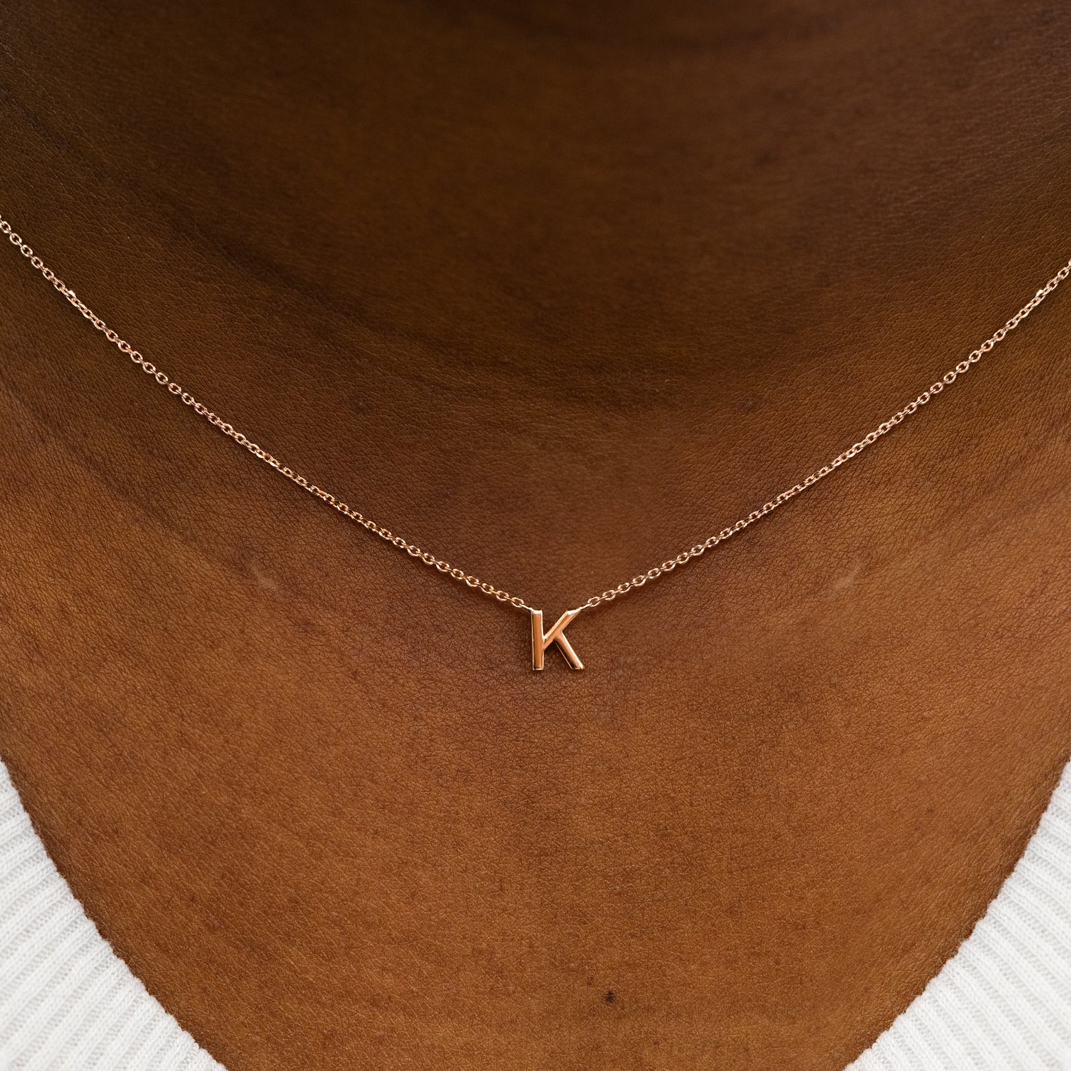Close up view of a model's neck wearing a 14k solid rose gold Block Initial Necklace in the letter K
