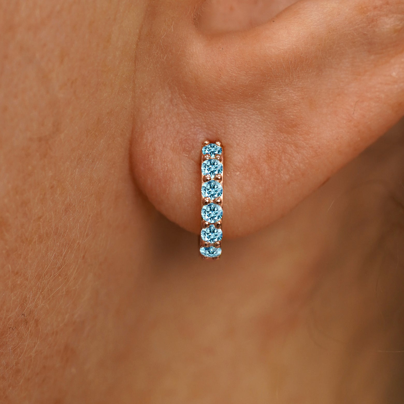 Close up view of a model's ear wearing a rose gold Small Light Blue Lab Diamond Huggie Hoop
