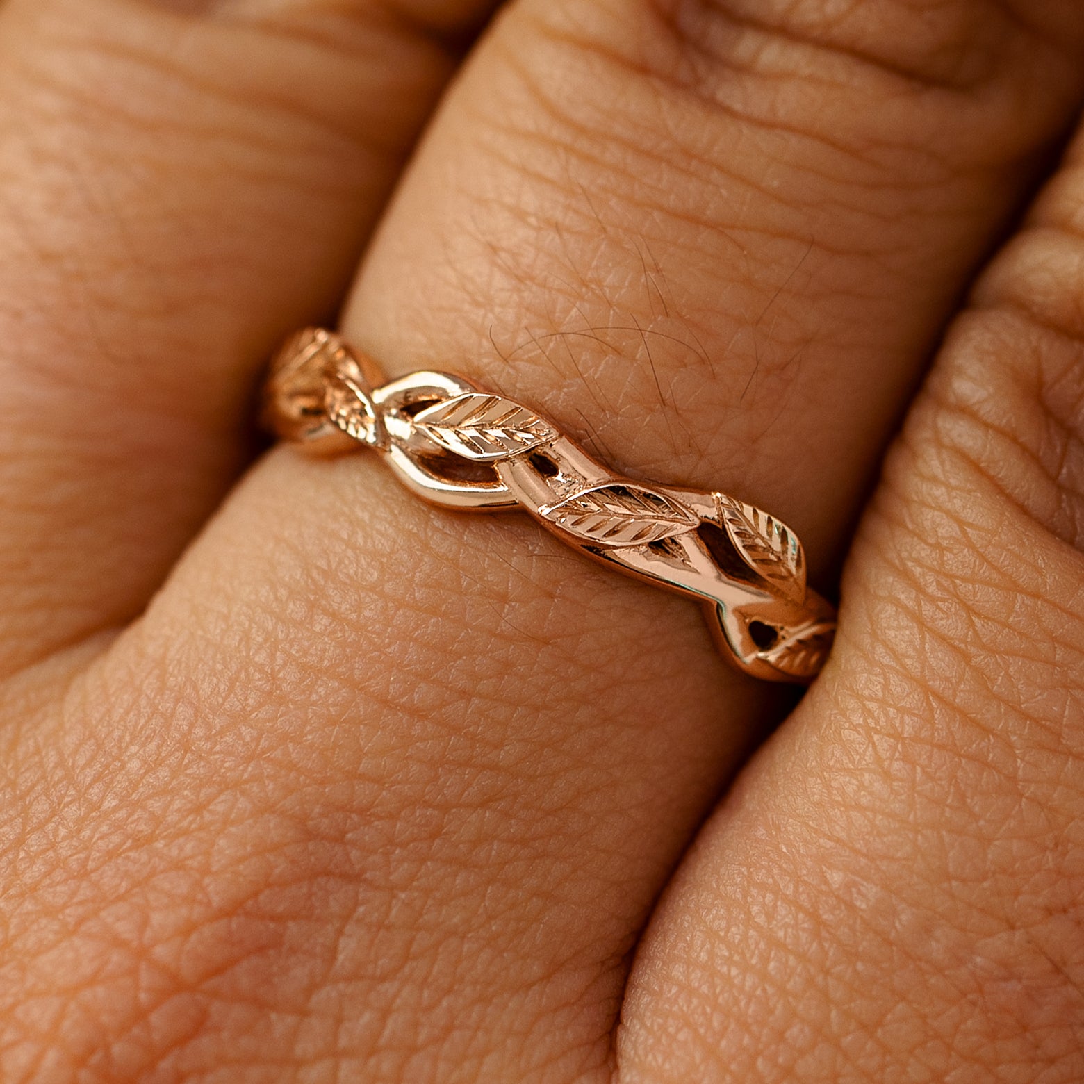 A solid 14k rose gold braided leaves and vines ring on a model's finger