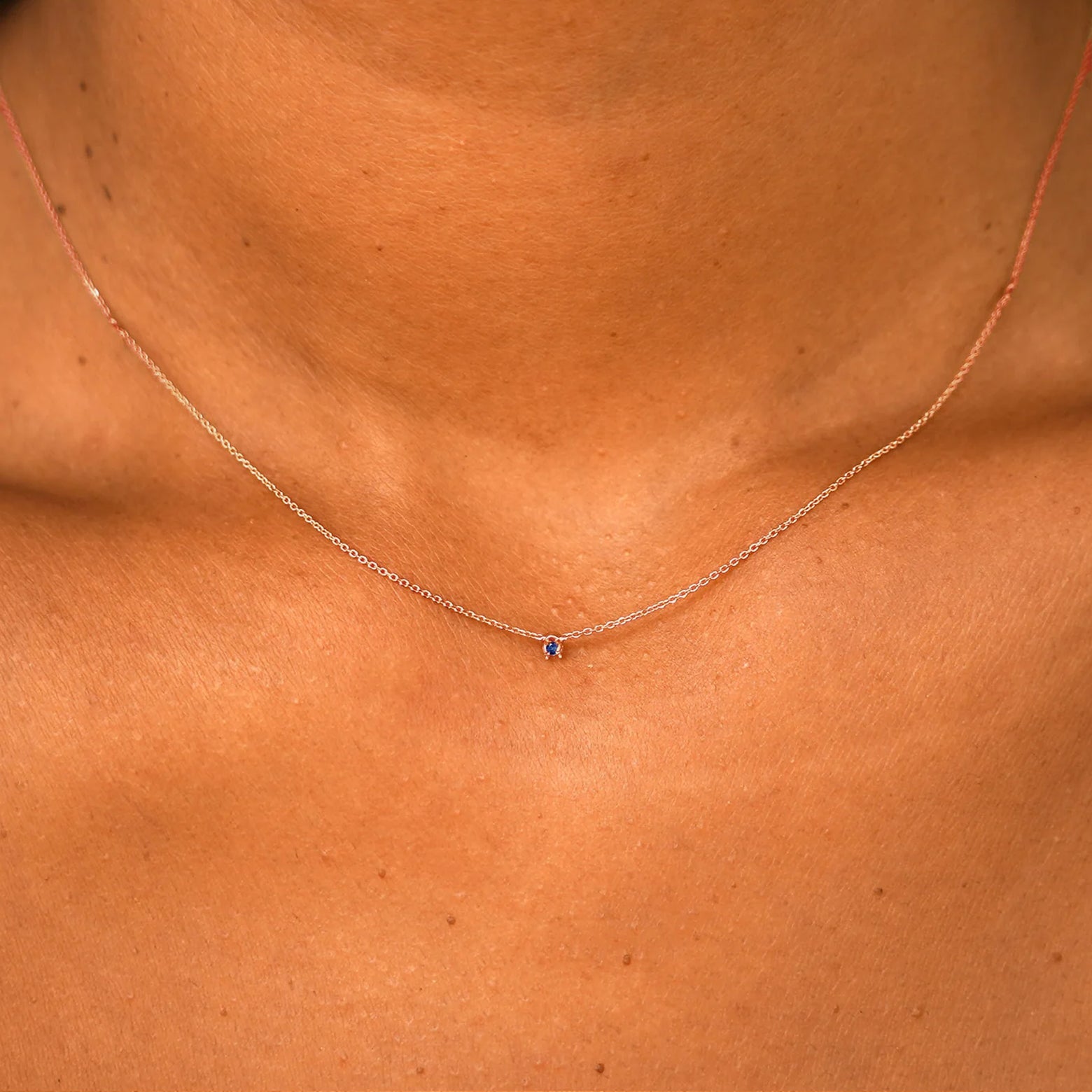 Close up view of a model's neck wearing a solid 14k rose gold Gemstone Cable Necklace in sapphire