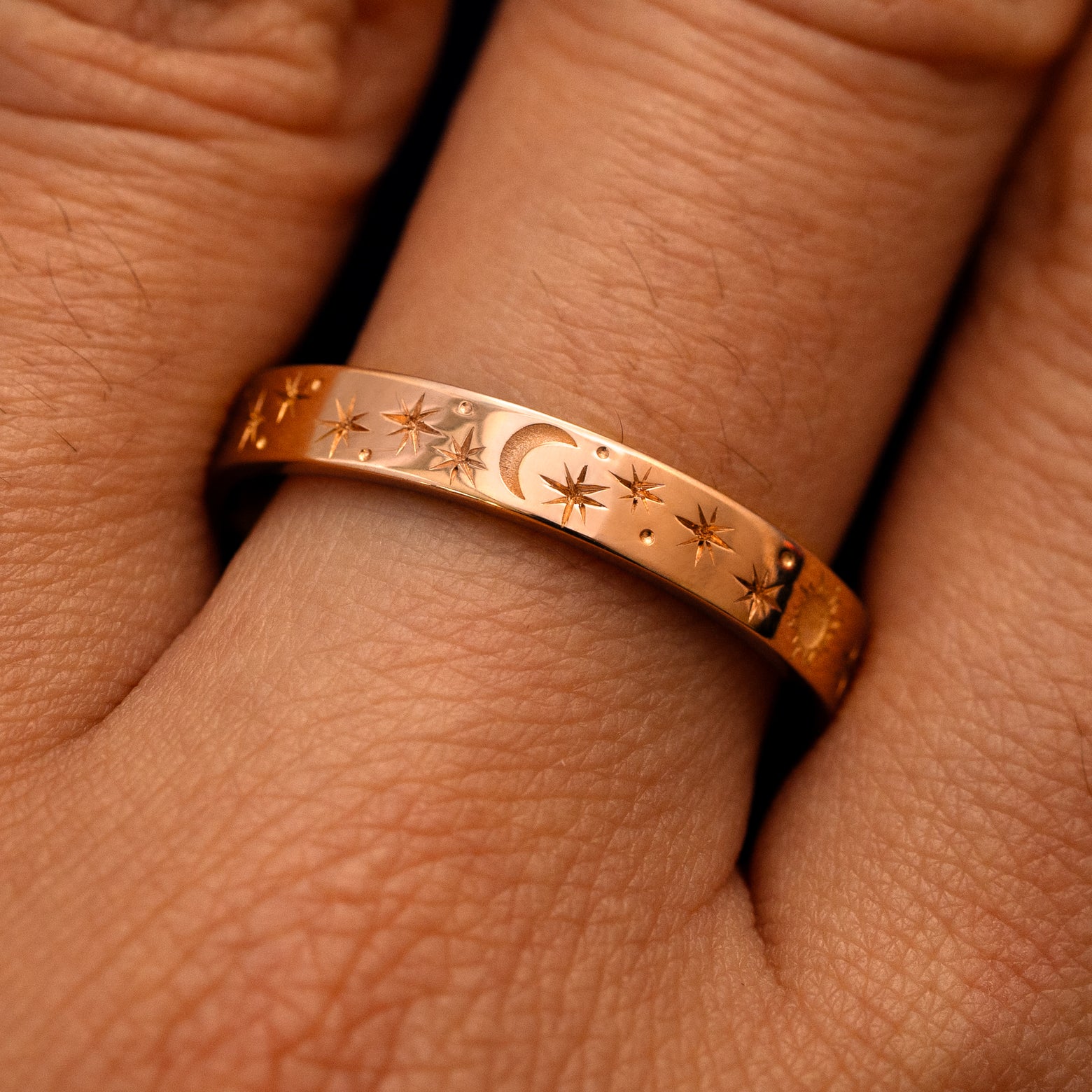 Close up view of a model's fingers wearing a 14k rose gold Industrial Sun Moon and Stars Band