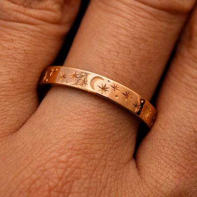 Close up view of a model's fingers wearing a 14k rose gold Industrial Sun Moon and Stars Band