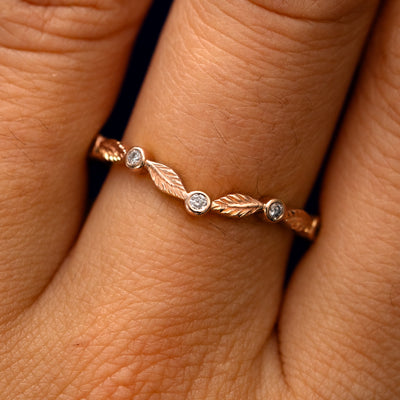 Close up view of a model's fingers wearing a 14k rose gold Chevron Leaves and Round Diamonds Band