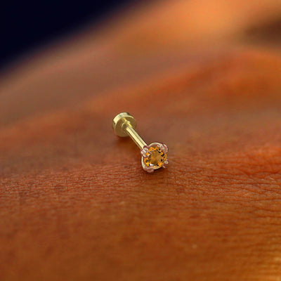 A solid 14k rose gold Citrine Flatback Piercing resting on the back of a model's hand