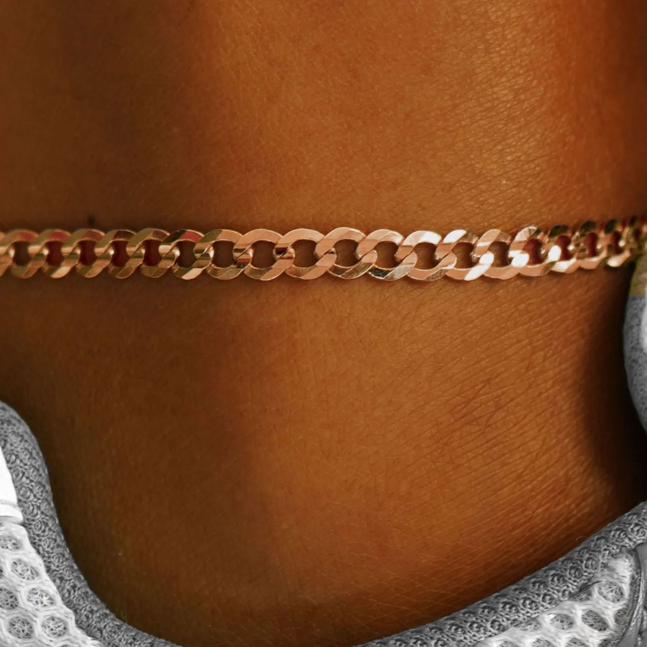 Close up view of a model's ankle wearing a 14k rose gold Curb Anklet