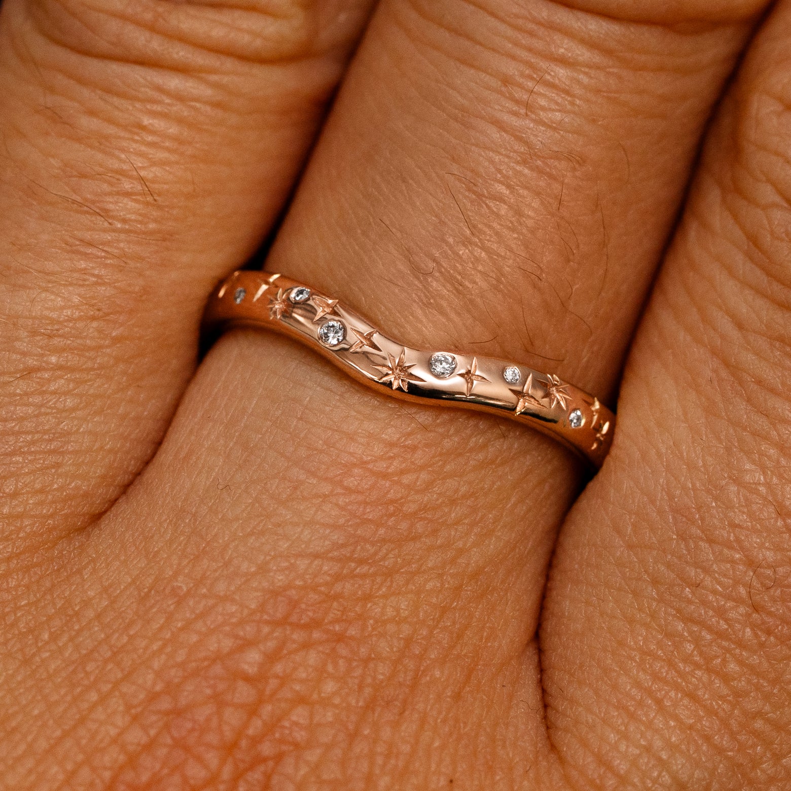 Close up view of a model's fingers wearing a 14k rose gold Curvy Chevron Diamond Stars Band
